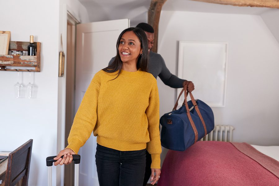 Short-Term Rental Insurance - Smiling Young Couple Opening the Door to a Vacation Rental and Carrying Luggage While Spending the Weekend Away From Home