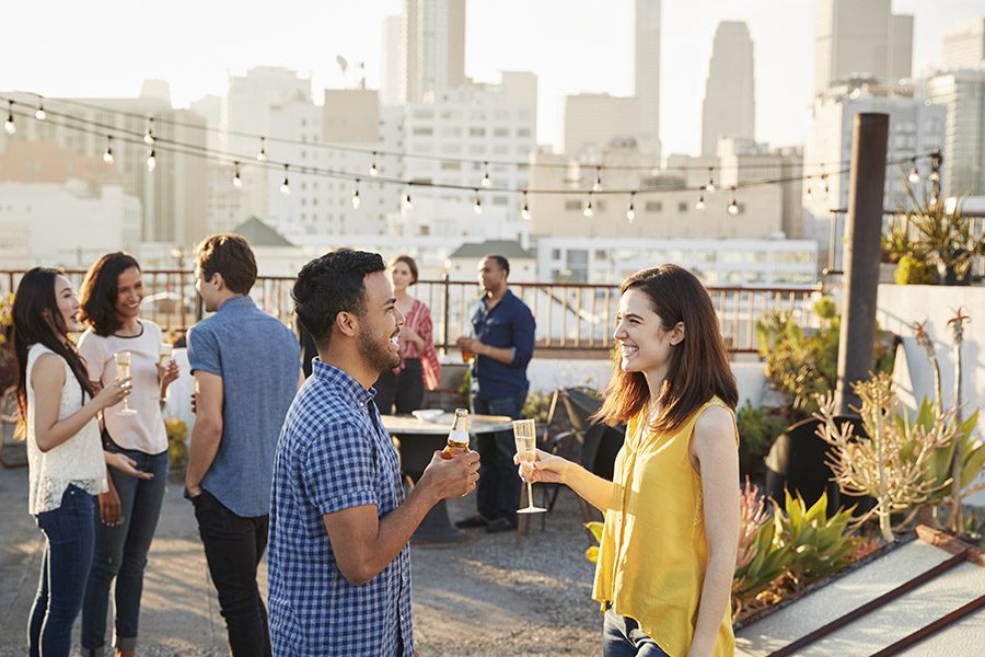 About Our Agency - A Group of People are Having a Party on the Roof of a Building With City Buildings in the Background on a Sunny Day