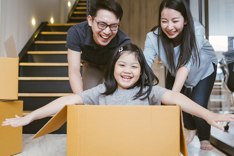 Personal Insurance - Happy Mother and Father Push Their Daughter While She Sits in a Cardboard Box as They Move into Their New Apartment